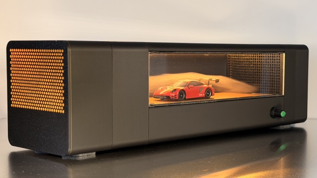 Seitliche Ansicht der Windkanal-Vitrine mit rotem Modellauto, Schalter und gelochtem Lüftungsgitter